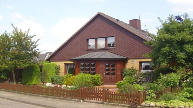 A two-story house with a brown roof, a front porch, and a wooden fence. - "haus Burck" Modern Retreat (Wankendorf)