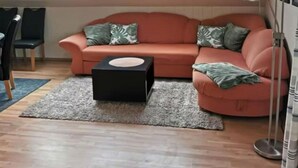 A cozy living room with a curved sofa, a small black ottoman, and a tall floor lamp. There are skylights above the sofa, and a chair is visible in the background. - "haus Burck" Modern Retreat (Wankendorf)