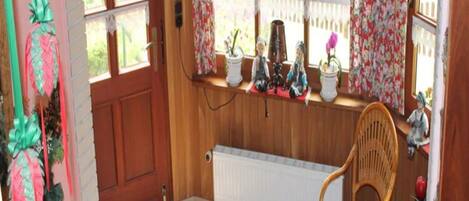 Una stanza accogliente con una porta in legno, un termosifone, una sedia in vimini e uno scaffale con oggetti decorativi.