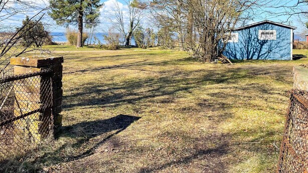 A fenced yard with a blue shed, trees, and a clear sky. - 5 Person Holiday Home in Borgholm (Borgholm)