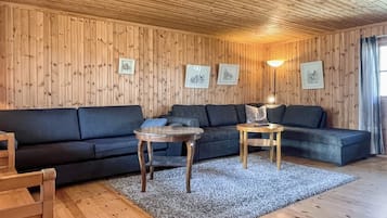 A wooden-paneled room with a sofa, two small tables, and framed pictures on the wall.