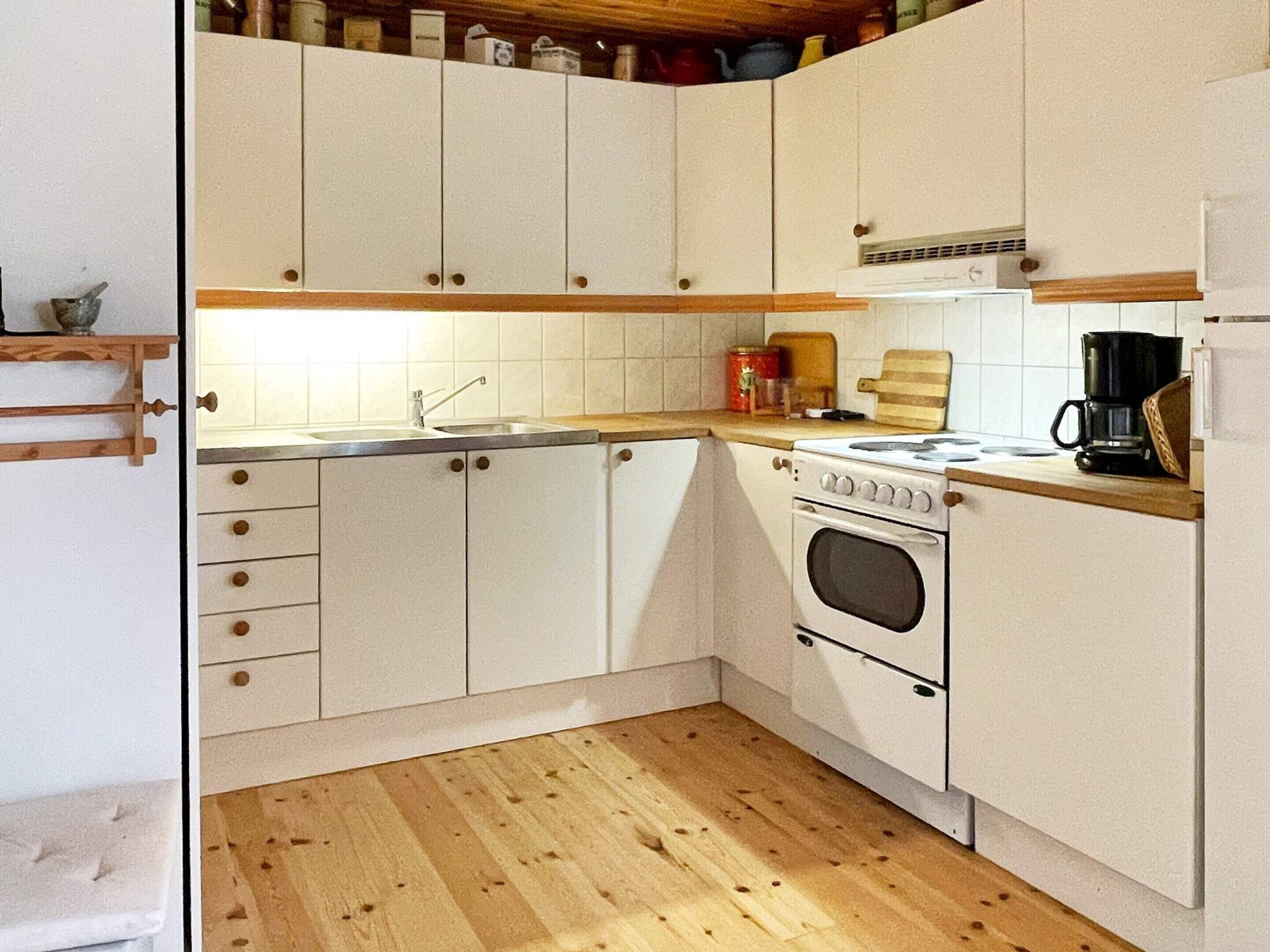 A kitchen with white cabinets, a wooden countertop, a stove, and a coffee maker.