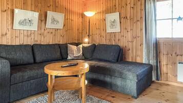 A cozy room with wooden walls, a sectional sofa, a round wooden coffee table, and framed pictures on the wall.