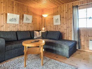 A cozy room with wooden walls, a sectional sofa, a round wooden coffee table, and framed pictures on the wall. - 5 Person Holiday Home in Borgholm (Borgholm)