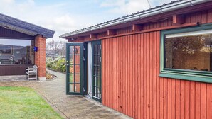 A red building with a green-framed window and a door, a brick pillar, and a small outdoor seating area with a table and chairs. - 2 Person Holiday Home in Skagen (Skagen)