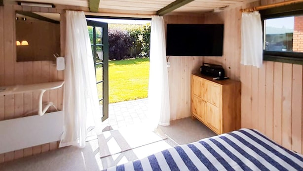 A bedroom with a bed, a wooden dresser, a television, and a bathroom with a shower and a toilet. - 2 Person Holiday Home in Skagen (Skagen)