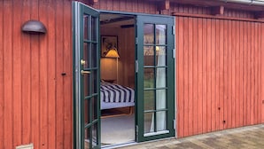 A red wooden building with a green door leading to a room with a bed and a lamp. - 2 Person Holiday Home in Skagen (Skagen)