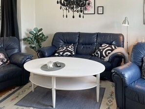A living room with a dark leather sofa, a white coffee table, and a potted plant.