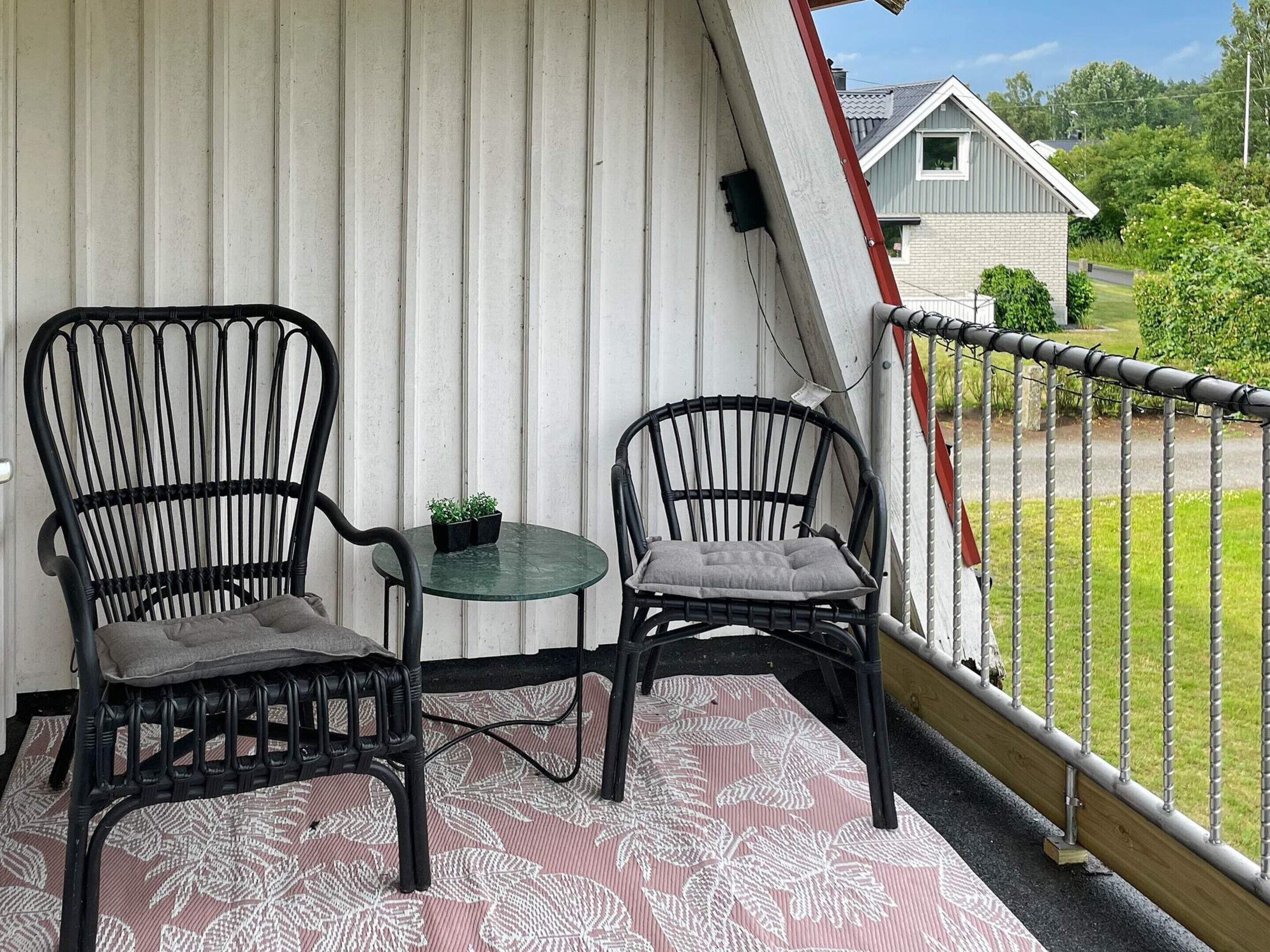 Ein Balkon mit zwei Stühlen, einem kleinen Tisch, einem Metallgeländer und Blick auf ein Haus und Grünflächen.