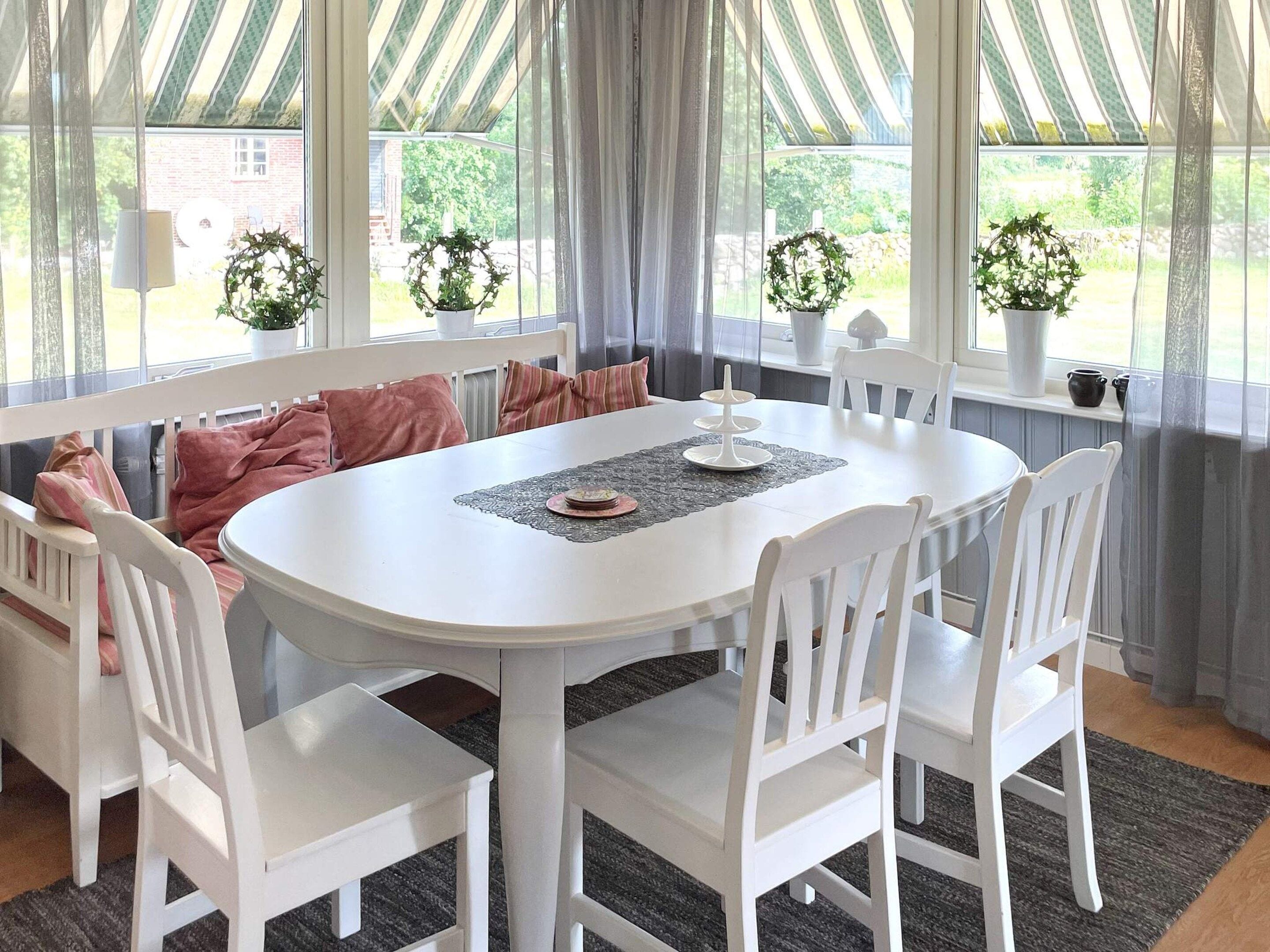 A dining area with a round table, white chairs, and a bench with cushions.