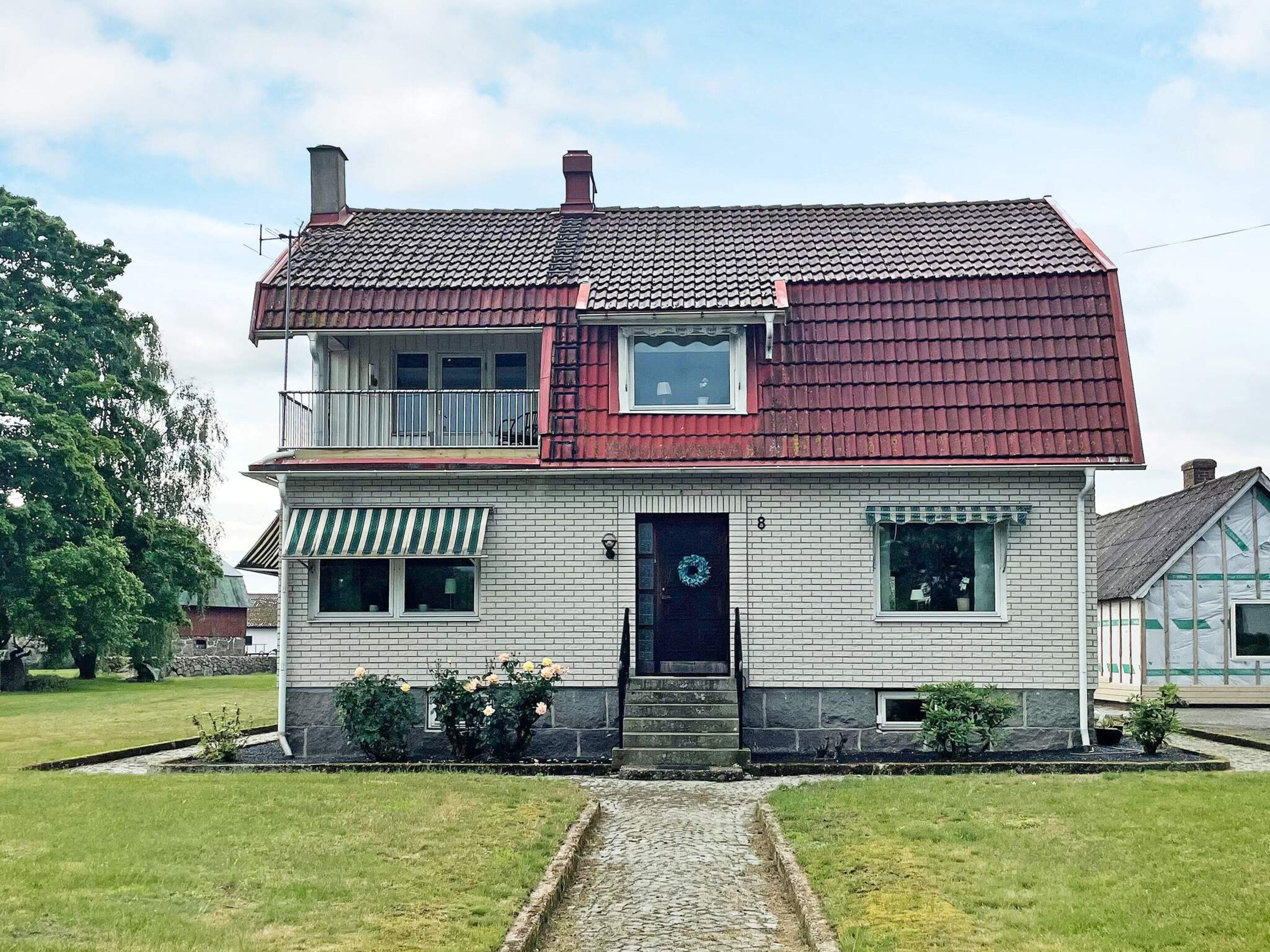A two-story house with a red-tiled roof, a front porch, and a small garden.