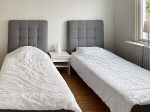 A twin room with two beds, a bedside table with a lamp, and a window with a view.