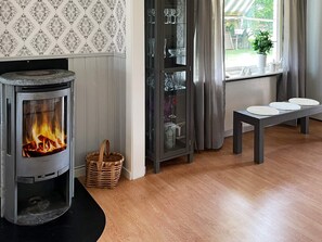 Una sala de estar con una chimenea de leña, un aparador de vidrio con cristalería, una cesta de mimbre y un banco con platos.