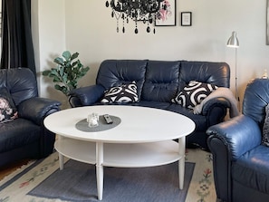 A living room with a dark leather sofa, a white coffee table, and a potted plant. - 4 Star Holiday Home in Solvesborg (Sölvesborg)