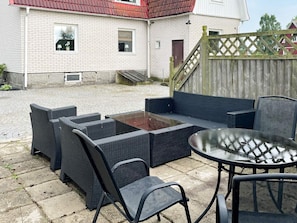 Un patio con mobiliario de mimbre, una mesa de vidrio y una valla de madera.