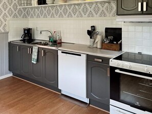 A kitchen with grey cabinets, a white dishwasher, a stove, and a coffee maker. - 4 Star Holiday Home in Solvesborg (Sölvesborg)