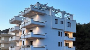 A multi-story modern building with balconies, a covered outdoor seating area, and a parking lot. - Arrei Hotel (Sarandë)