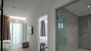 A modern hotel room with a glass shower enclosure, a bed with a small bedside table, and a seating area with a chair and ottoman. - Arrei Hotel (Sarandë)