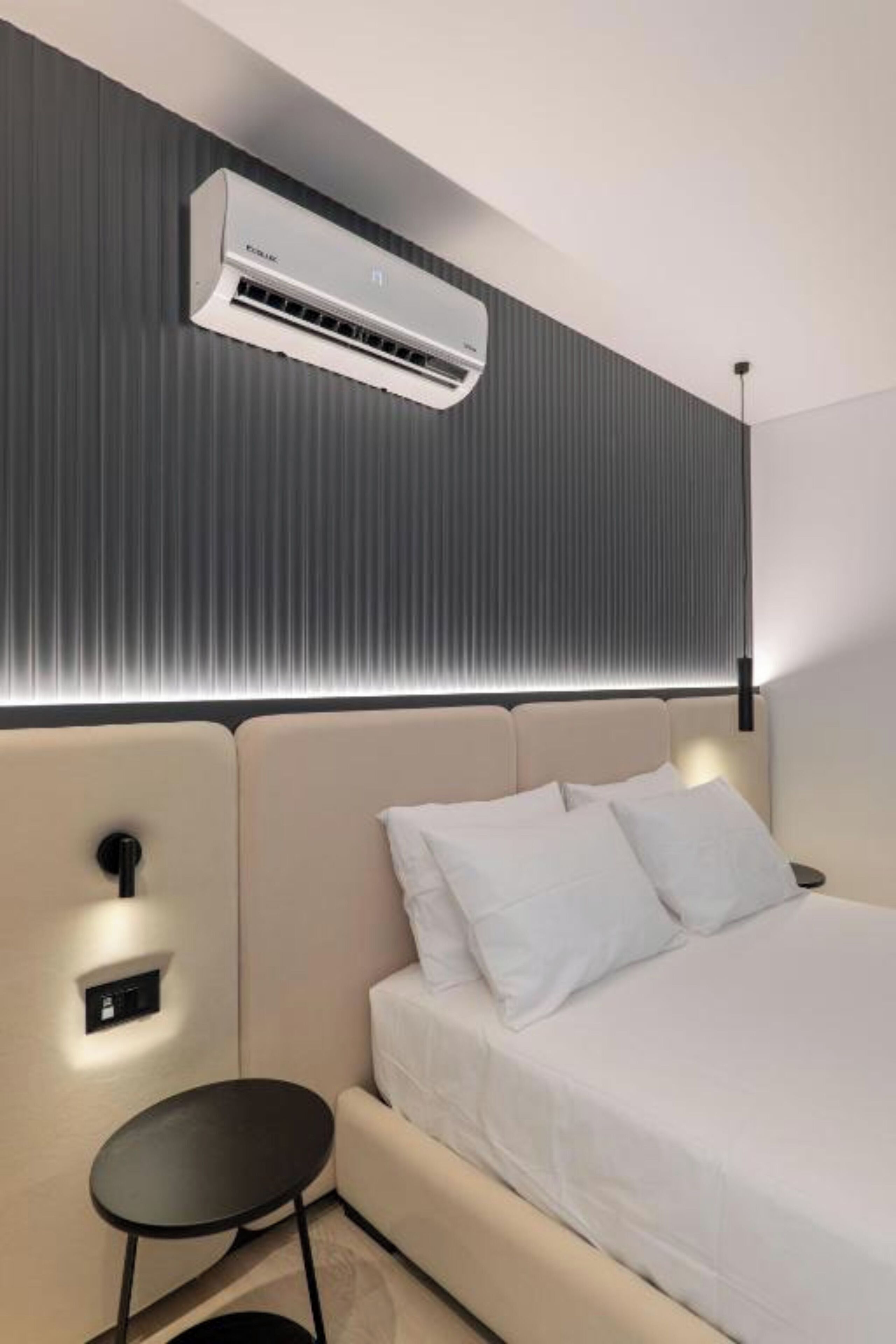 A modern hotel room with a bed, bedside table, and an air conditioning unit mounted on the wall.