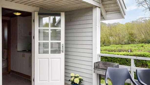 A wooden deck with a white door, a blue flower pot, and two chairs. - 4 Star Holiday Home in Asperup (Middelfart)