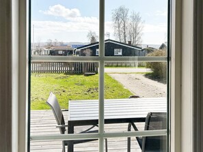A view through a window of a wooden deck with a table and chairs, a grassy area, and a wooden fence. - 4 Person Holiday Home in Skummeslovsstrand (Skummesloevsstrand)