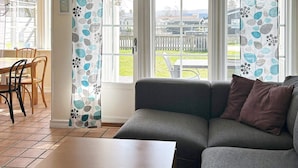 A living room with a grey sofa, a wooden coffee table, and a view of a backyard through large windows. - 4 Person Holiday Home in Skummeslovsstrand (Skummesloevsstrand)