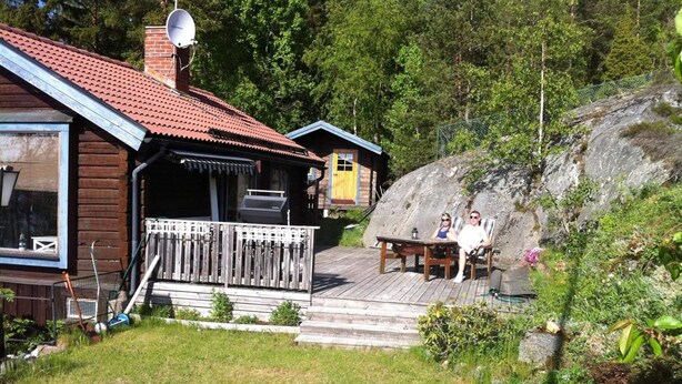 Une cabane en bois avec un toit recouvert de tuiles rouges, une terrasse et un espace barbecue.