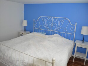 A bed with a white metal frame and headboard, flanked by two bedside tables with lamps, in a room with blue walls and wooden flooring. - 4 Star Holiday Home in Musko (Muskö)