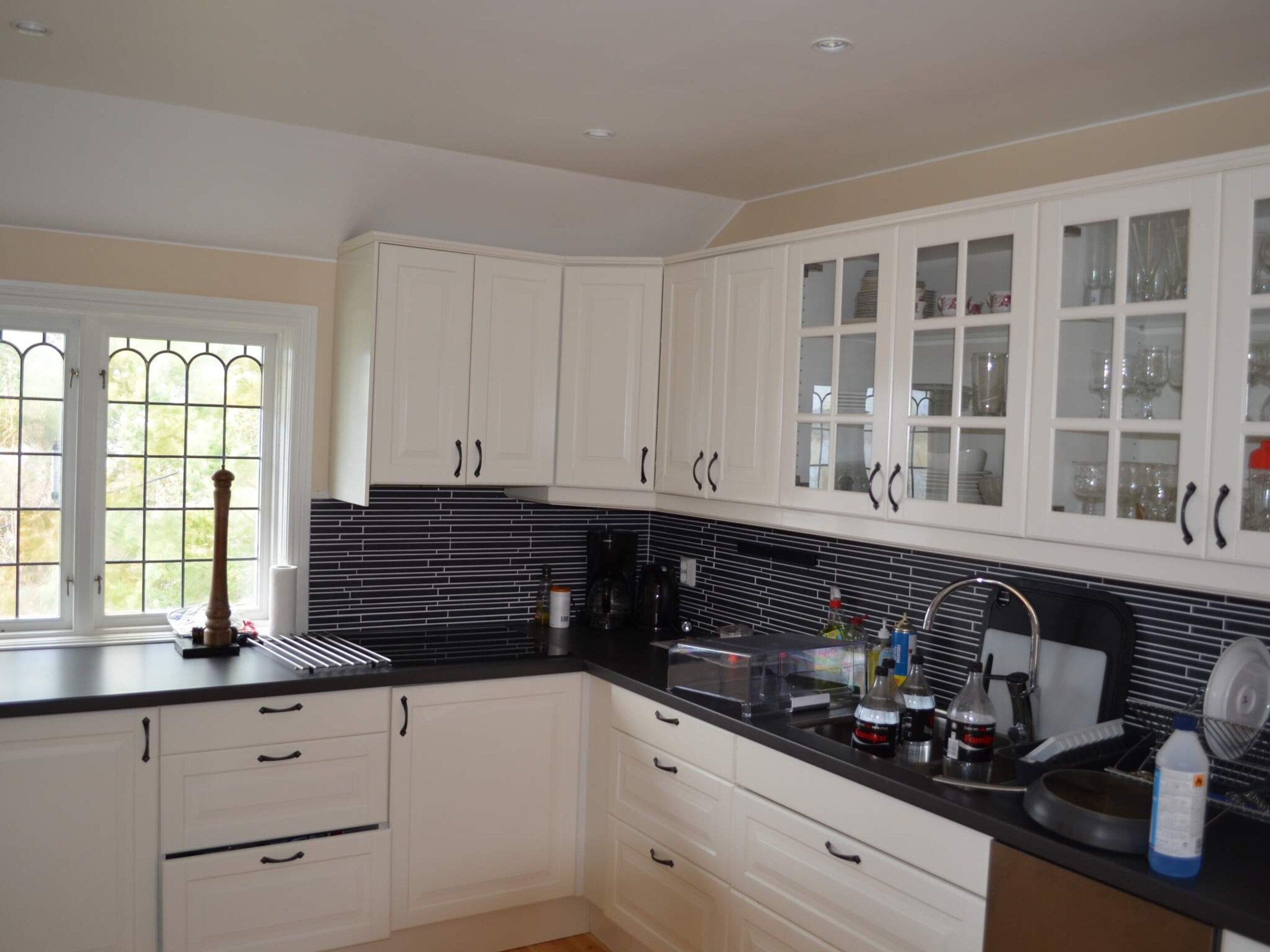 A kitchen with white cabinets, a black countertop, and a window with a view of greenery.