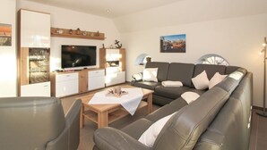 A modern living room with a sofa, TV, wooden cabinet, and a dining table. - Anchor Claw Comfortable Holiday Residence (Krummhoern)