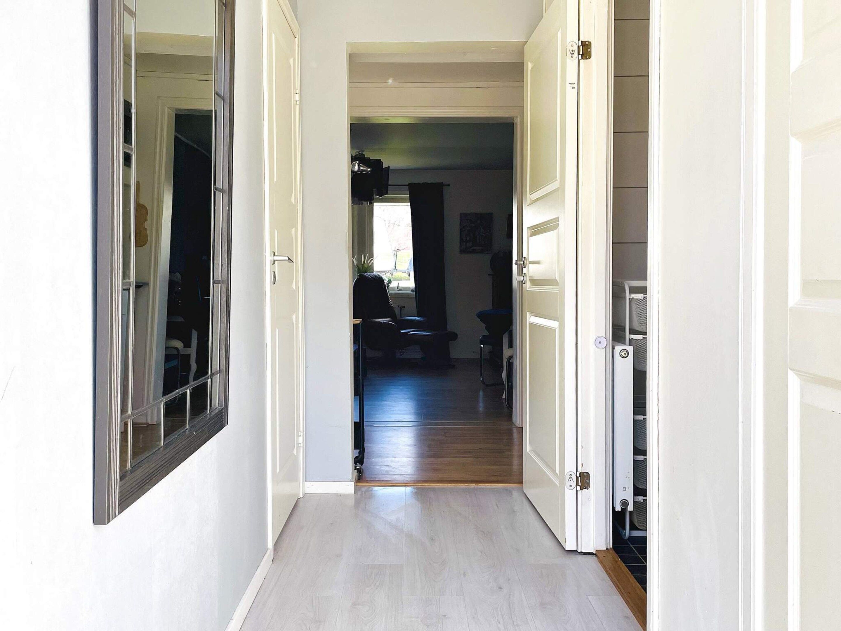 Un passadís amb una porta que condueix a una habitació amb finestra, una cadira i un taulell.