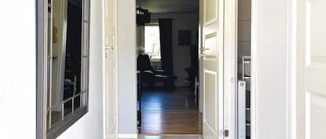 A hallway with a door leading to a room with a window, a chair, and a table.