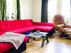 A living room with a red sofa, a brown leather chair, a small table with a decorative item, and a patterned throw on the sofa. - 4 Person Holiday Home in Dals Rostock (Dals Rostock)