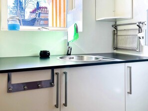 A kitchen with a stainless steel sink, a window with a view of trees and buildings, and a metal rack with utensils. - 4 Person Holiday Home in Dals Rostock (Dals Rostock)