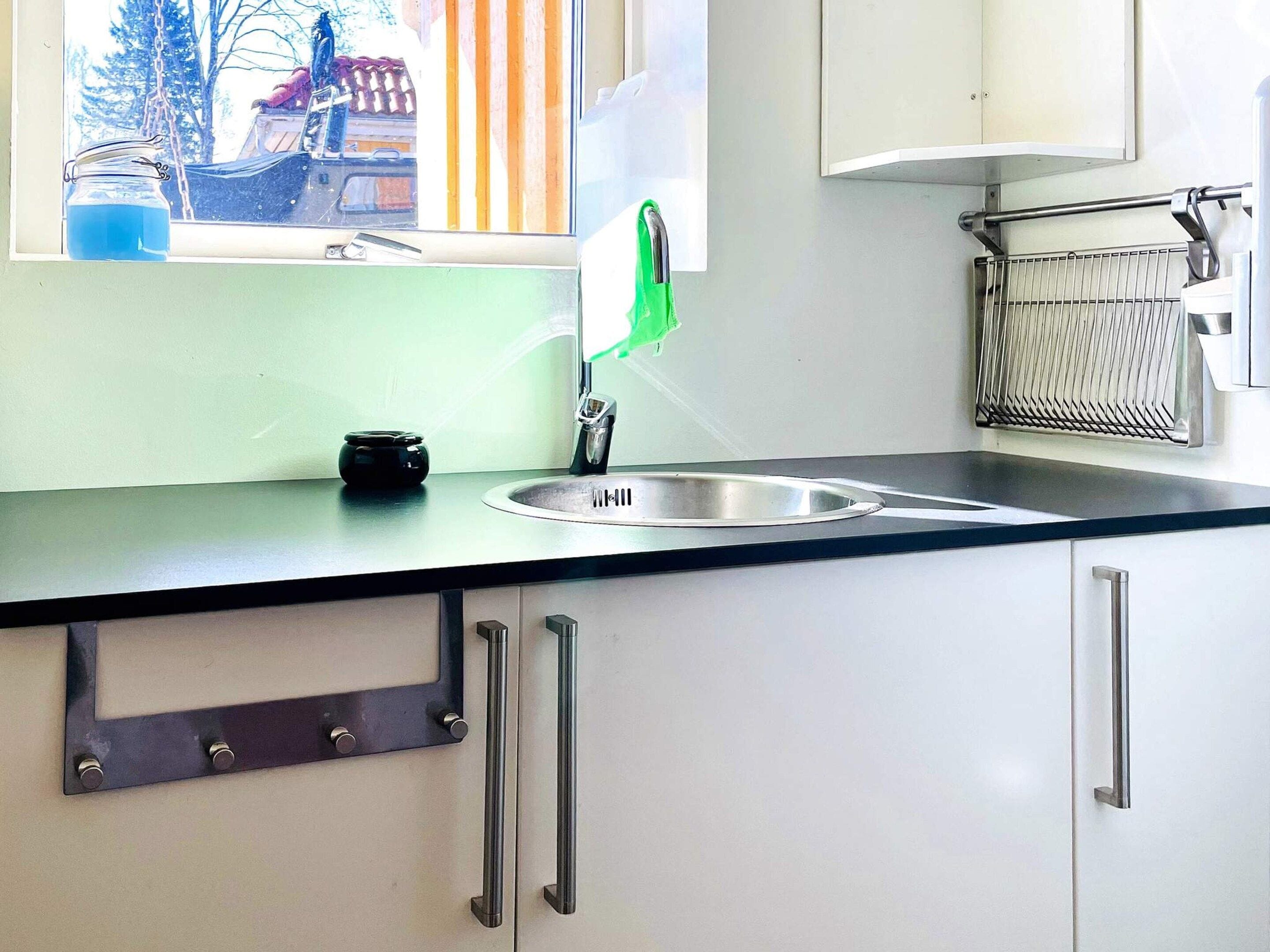A kitchen with a stainless steel sink, a window with a view of trees, and a metal rack.