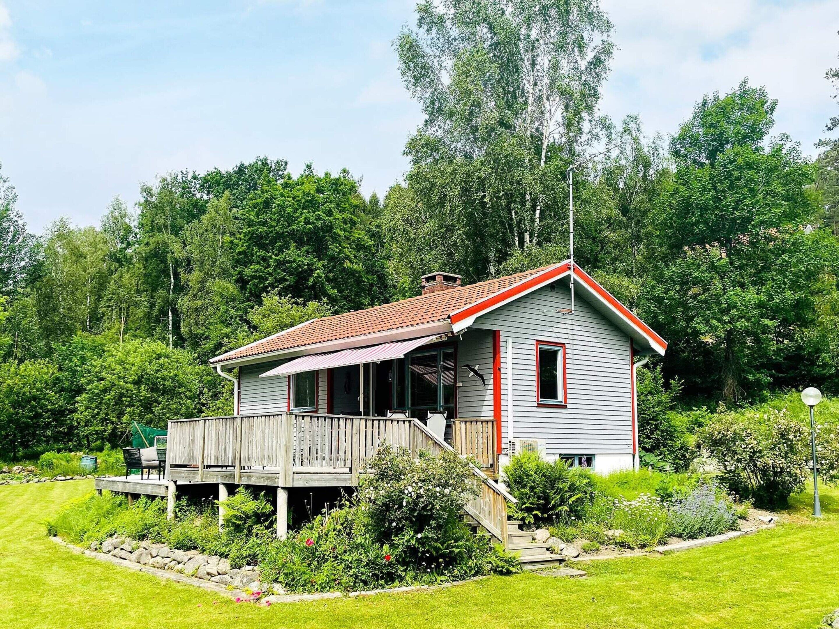Ein kleines, einstöckiges Haus mit rotem Dach und weißer Fassade, umgeben von einem gepflegten Garten und Bäumen.