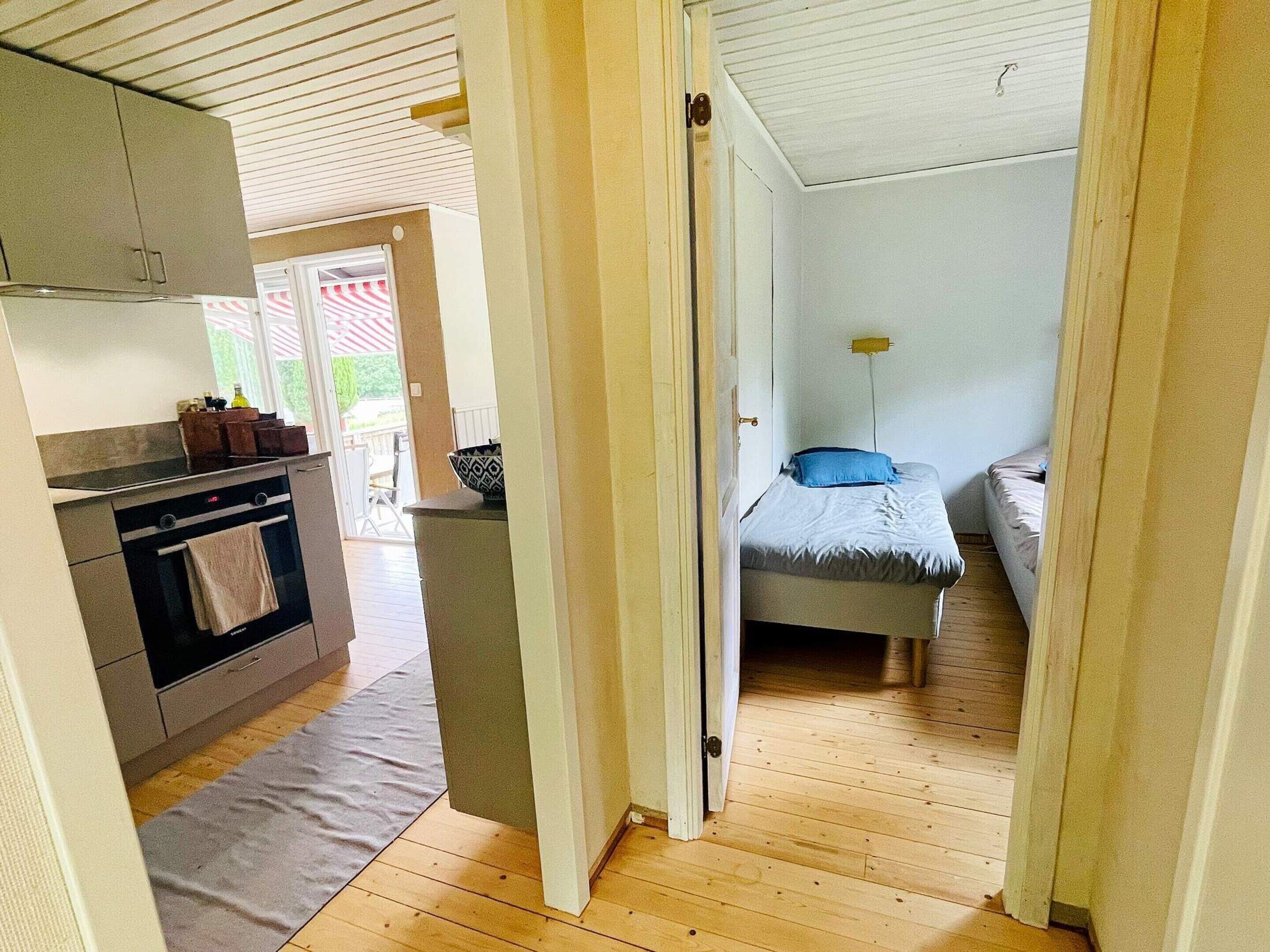 A compact room with a kitchenette on one side, a bed with a blue pillow, and a small bedside table.