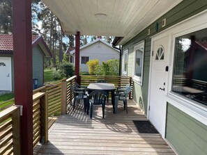 En inglasad veranda med ett bord och stolar, ett träräcke och ett hus med en garageport.