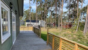 A wooden deck leading to a building with a green exterior and a fenced yard with trees and a small shed. - 4 Star Holiday Home in Monsteras (Monsteras)