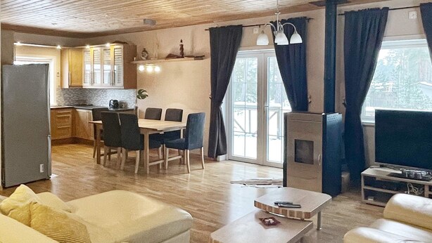 A living room with a sofa, a coffee table, and a TV. There is a dining area with a table and chairs. A kitchen with cabinets and a refrigerator is visible. - 4 Star Holiday Home in Monsteras (Monsteras)