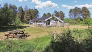 Une cabane dotée d’une véranda, entourée d’un champ verdoyant et d’arbres.