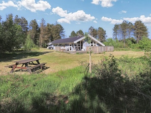 A cabin with a porch, surrounded by a grassy field and trees. - 4 Star Holiday Home in Albaek (Aalbaek)