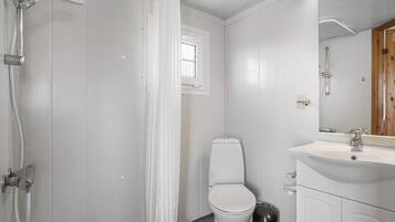 A bathroom with a shower, toilet, sink, and a trash bin.