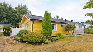 A yellow mobile home with a fenced yard, surrounded by greenery and trees.