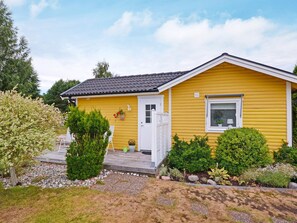 Ett gult, enplanshus med en vit dörr, en liten veranda och ett fönster med en blomma i.
