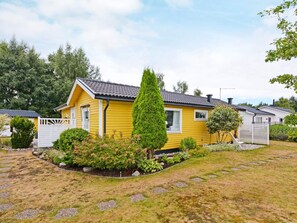 Ett gult husvagn med en inhägnad trädgård, omgivet av träd och buskar.