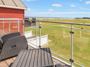 A balcony with outdoor furniture, a red building, and a view of the beach.