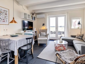 A modern living room with a dining area, a sofa, a TV, and a view through a glass door. - 6 Person Holiday Home in Hadsund (Hadsund)