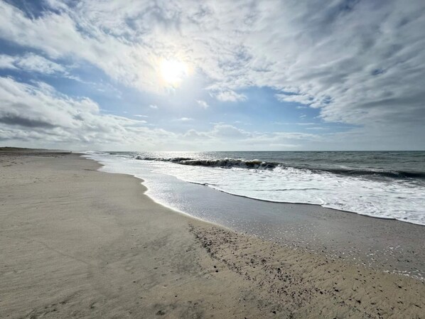 A beach with waves, a clear sky, and the sun.