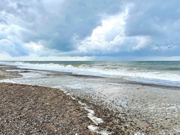 A beach with pebbles and waves, under a cloudy sky.